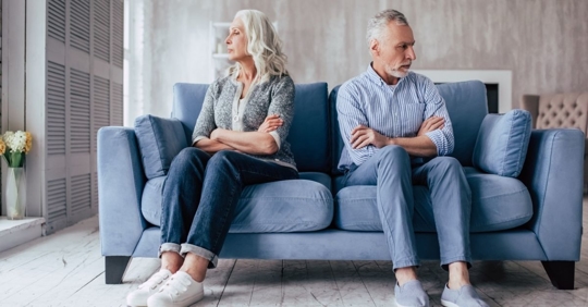 Older couple on a couch with arms crossed and looking away from each other