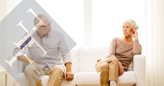 Older couple sitting on a couch far away from each other.