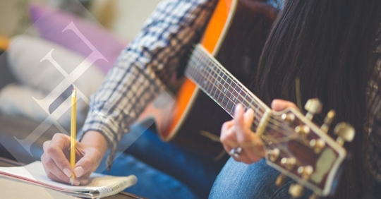 Image of a man writing music while holding a guitar